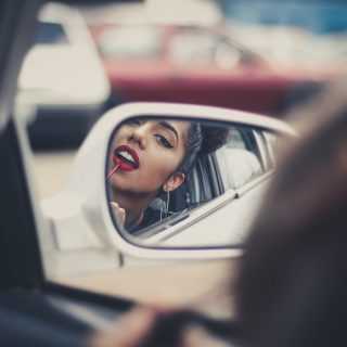 Девушка красит губы в зеркальце машины