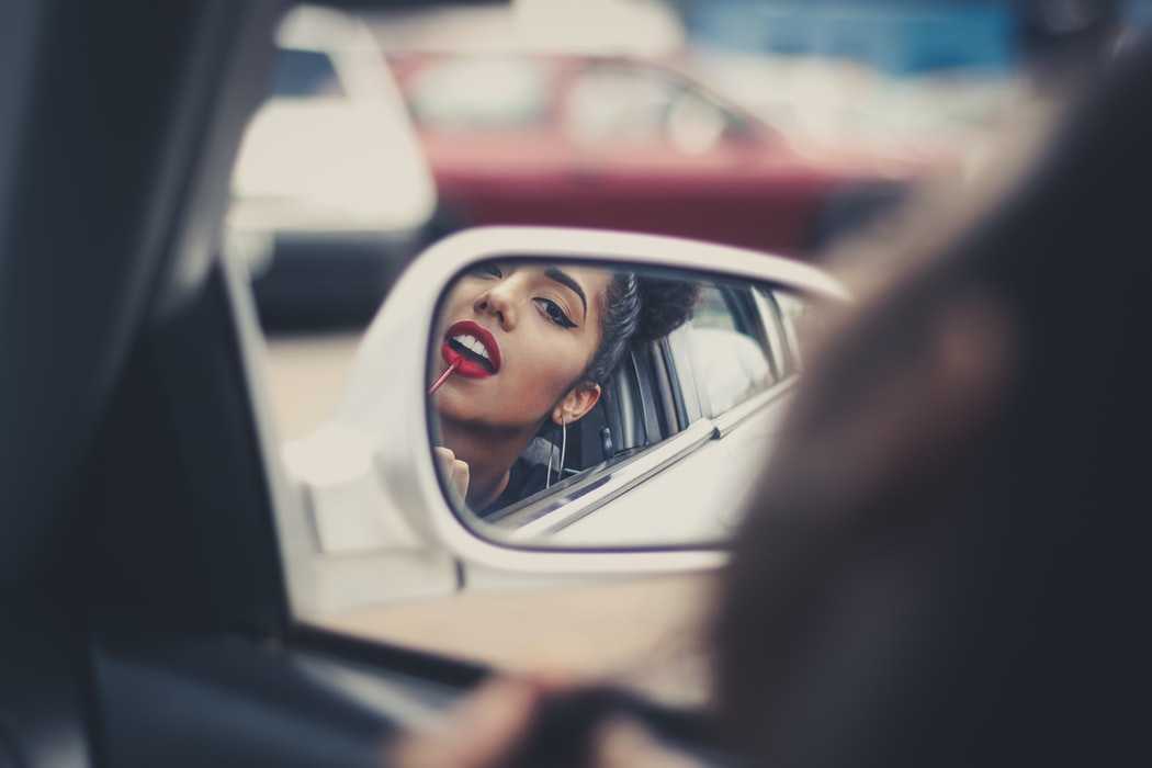 Девушка красит губы в зеркальце машины